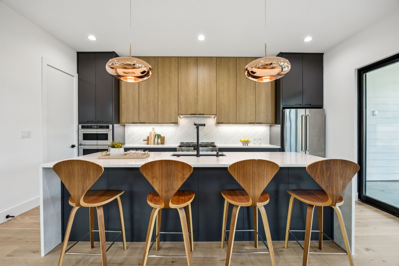 Four modern wooden stools with backs lined up against a kitchen island
