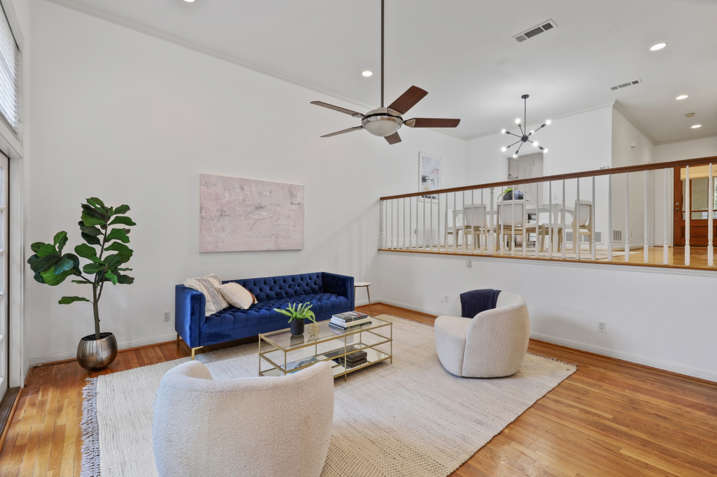 An open concept living room with a blue velvet couch and two white chairs